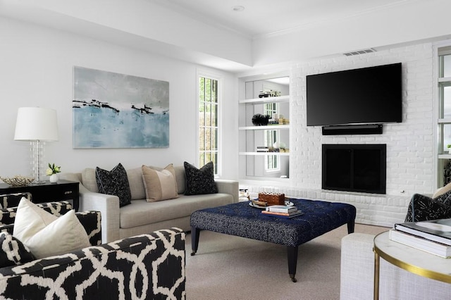 carpeted living area featuring a brick fireplace, built in shelves, visible vents, and crown molding