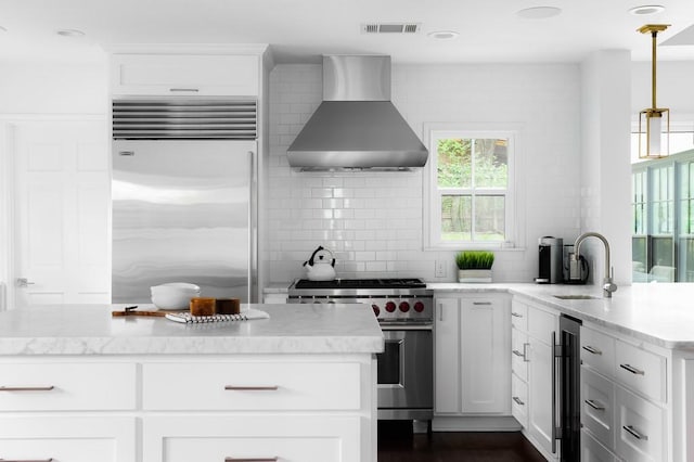 kitchen featuring tasteful backsplash, visible vents, high end appliances, wall chimney exhaust hood, and a sink