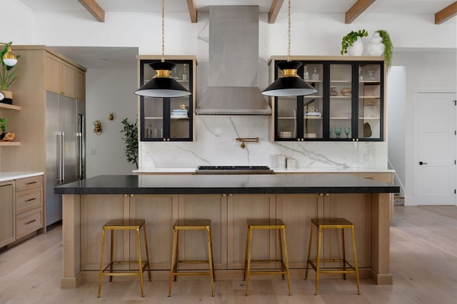 kitchen featuring high end fridge, wall chimney range hood, backsplash, and open shelves