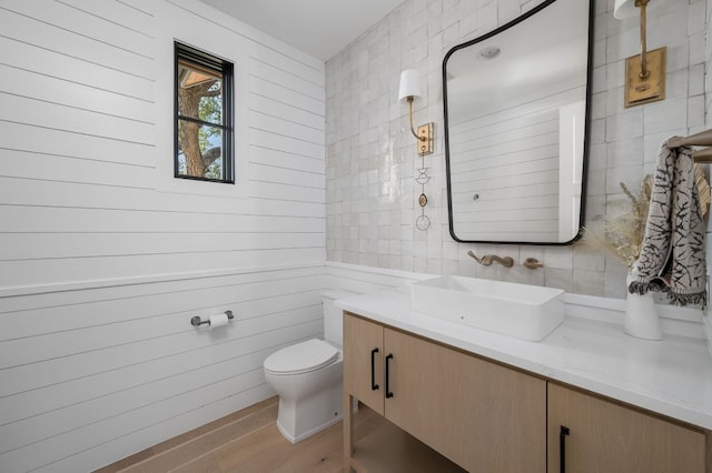 bathroom with toilet, wood finished floors, tile walls, and vanity