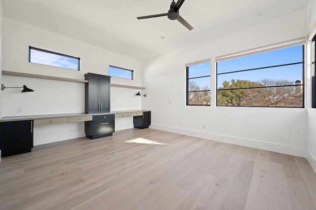 unfurnished office featuring a healthy amount of sunlight, light wood finished floors, baseboards, and built in desk