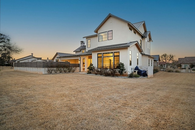 back of property at dusk with a yard, a standing seam roof, metal roof, and fence