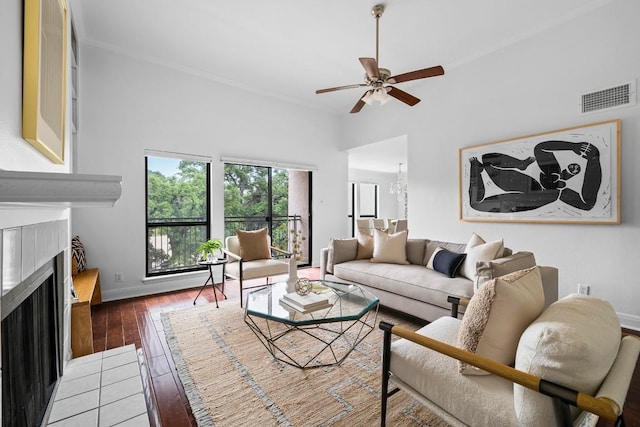 living area featuring visible vents, baseboards, hardwood / wood-style flooring, a fireplace with flush hearth, and ceiling fan with notable chandelier