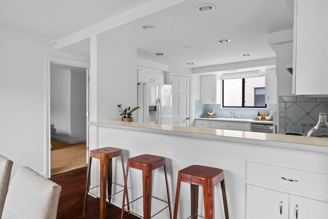 kitchen featuring light countertops, a kitchen bar, refrigerator with ice dispenser, and white cabinetry