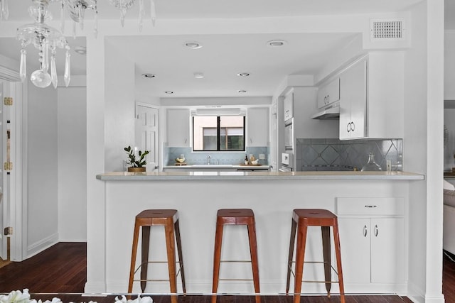 kitchen with under cabinet range hood, white cabinetry, visible vents, light countertops, and dark wood finished floors