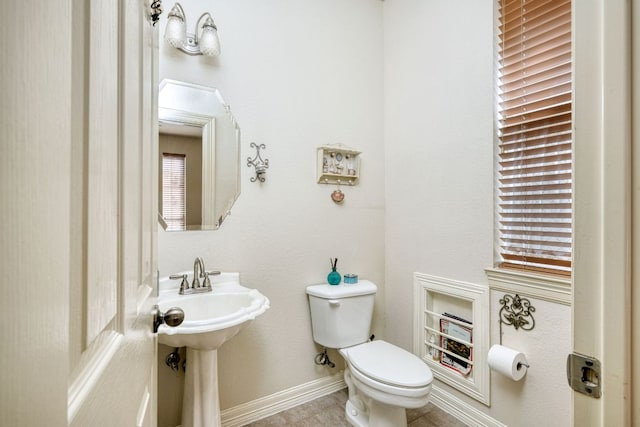 half bathroom featuring toilet, tile patterned flooring, baseboards, and a sink