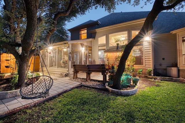 exterior space featuring fence, a sunroom, roof with shingles, a lawn, and a patio area