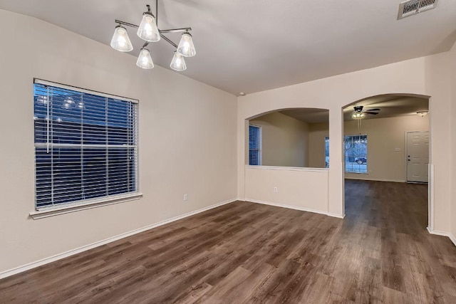 empty room featuring visible vents, arched walkways, dark wood finished floors, baseboards, and ceiling fan