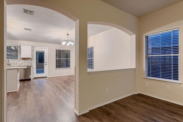 unfurnished room featuring a notable chandelier, baseboards, visible vents, and wood finished floors