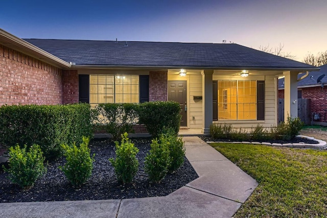 exterior entry at dusk with brick siding, roof with shingles, and a porch