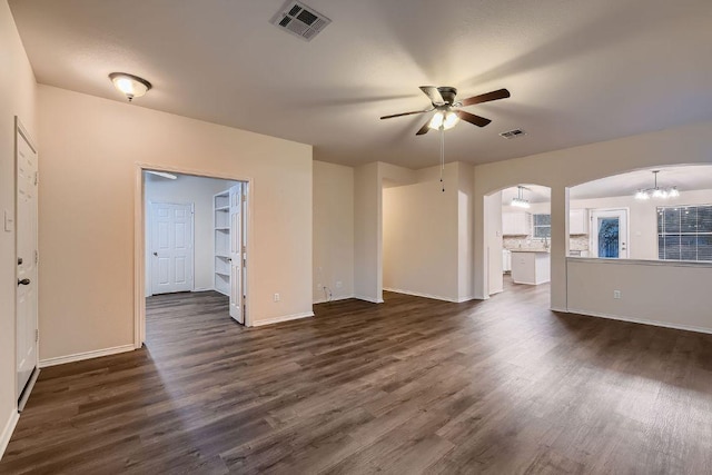 unfurnished living room with ceiling fan, visible vents, arched walkways, and dark wood-type flooring