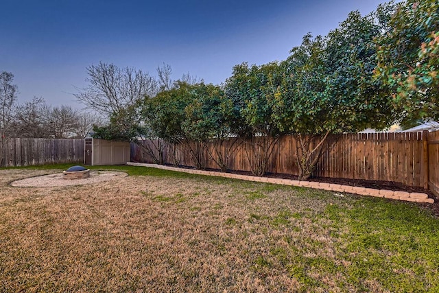 view of yard with an outdoor fire pit, a fenced backyard, a storage unit, and an outbuilding