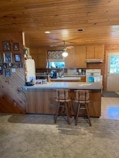 kitchen with a breakfast bar area, under cabinet range hood, stove, wood ceiling, and light countertops