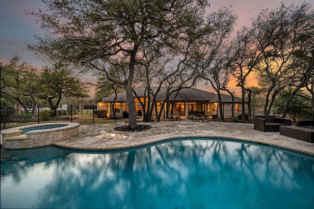 pool at dusk featuring a patio area, fence, a fenced in pool, and an in ground hot tub