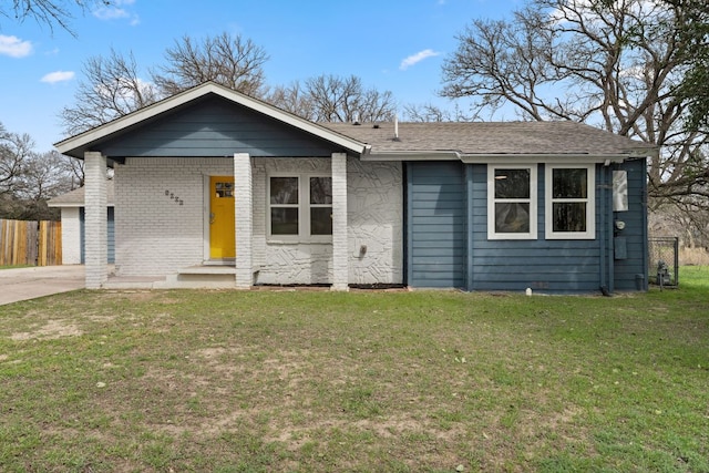 view of front of home with a shingled roof, brick siding, fence, and a front lawn