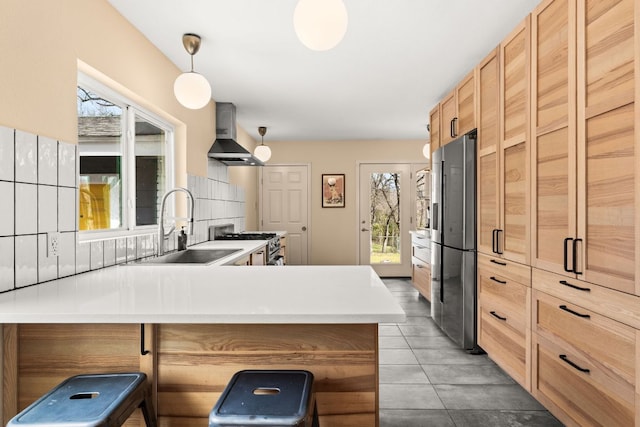 kitchen featuring stainless steel appliances, backsplash, a sink, a peninsula, and wall chimney exhaust hood