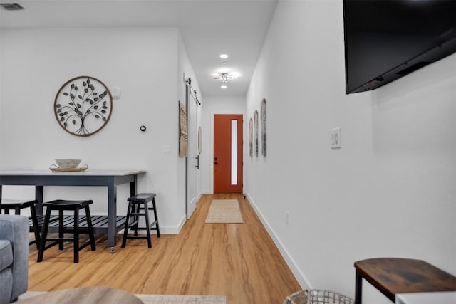 hall with wood finished floors, visible vents, baseboards, and a barn door