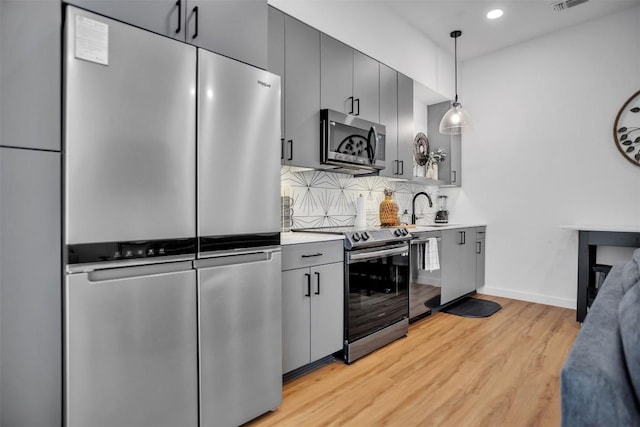 kitchen with stainless steel appliances, a sink, backsplash, light wood finished floors, and decorative light fixtures