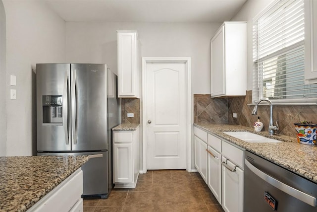 kitchen featuring stainless steel appliances, decorative backsplash, white cabinets, a sink, and light stone countertops