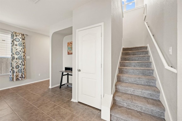 stairway with a healthy amount of sunlight, baseboards, arched walkways, and tile patterned floors