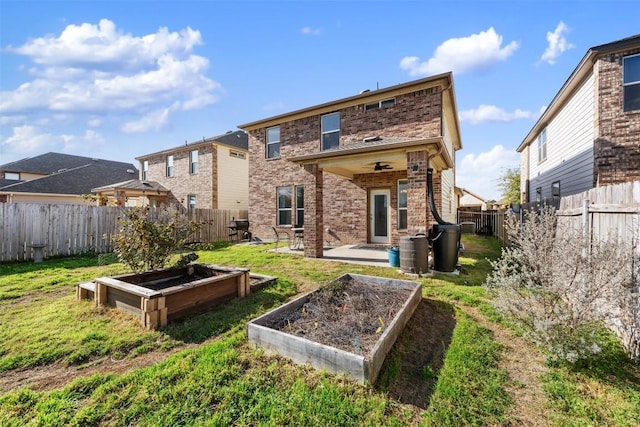 back of house featuring a garden, brick siding, a fenced backyard, and a lawn