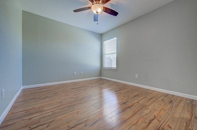 spare room with wood finished floors, a ceiling fan, and baseboards