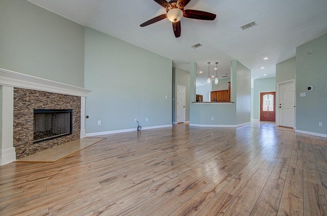 unfurnished living room featuring ceiling fan, a fireplace, visible vents, baseboards, and light wood-style floors