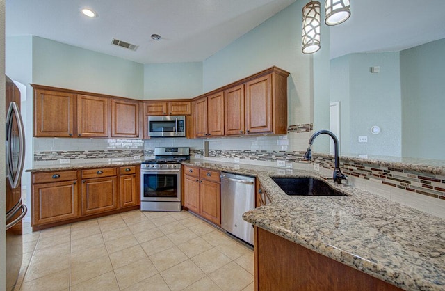 kitchen featuring stainless steel appliances, a sink, visible vents, brown cabinets, and light stone countertops