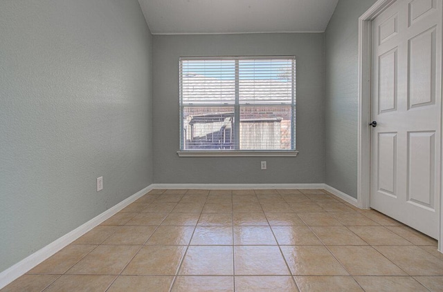 empty room with light tile patterned floors, a textured wall, and baseboards