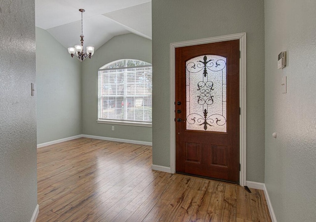 entryway featuring a textured wall, vaulted ceiling, a chandelier, baseboards, and hardwood / wood-style flooring