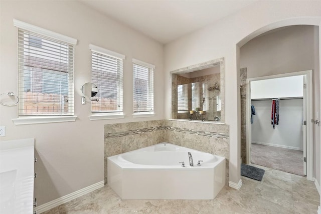 full bathroom with vanity, baseboards, a spacious closet, a tile shower, and a bath