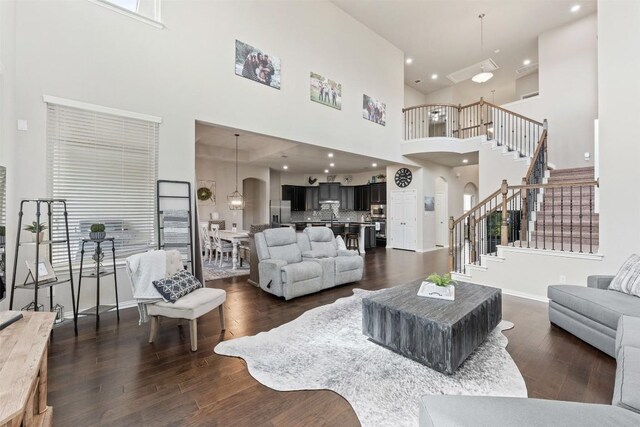 living area with arched walkways, dark wood finished floors, recessed lighting, stairway, and baseboards