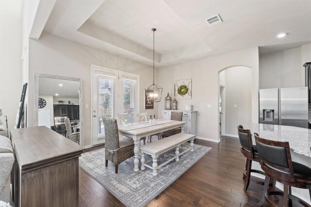 dining area with dark wood-style floors, arched walkways, a raised ceiling, visible vents, and baseboards