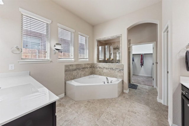 bathroom with vanity, baseboards, a tile shower, a bath, and a walk in closet