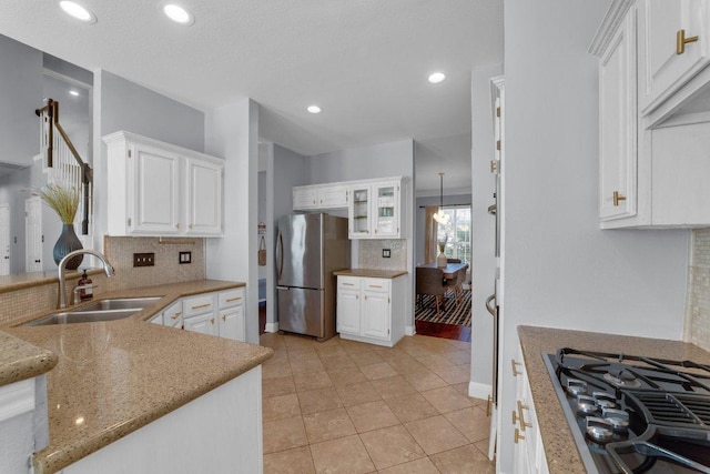 kitchen with black gas cooktop, a sink, white cabinets, backsplash, and freestanding refrigerator