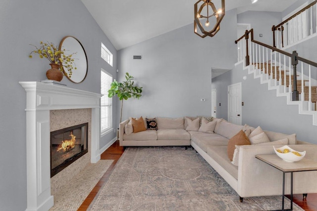 living area with a chandelier, a fireplace with flush hearth, wood finished floors, visible vents, and stairs