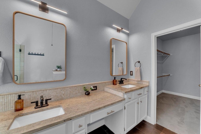 full bath with vanity, baseboards, a spacious closet, decorative backsplash, and a stall shower