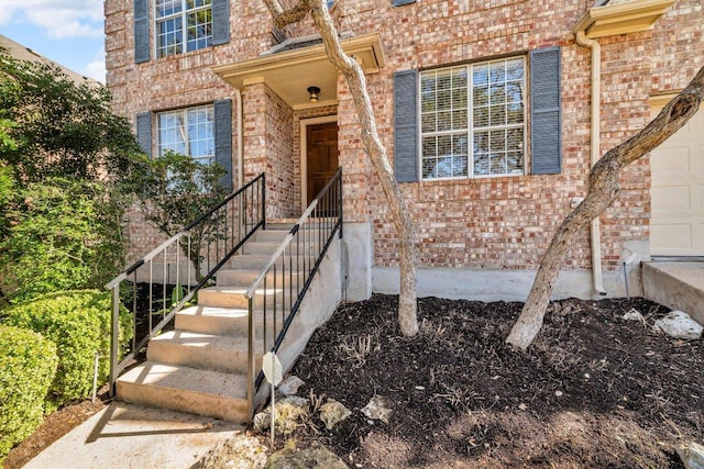 view of exterior entry featuring a garage and brick siding