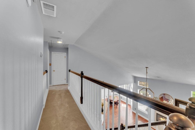 hallway featuring light colored carpet, lofted ceiling, visible vents, and an upstairs landing