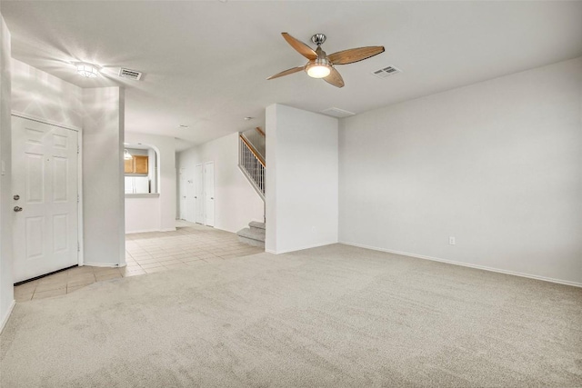 carpeted empty room with visible vents, stairway, a ceiling fan, and tile patterned floors