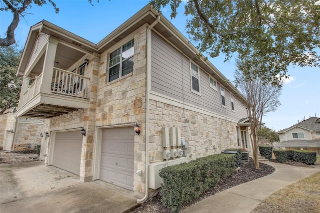 view of side of home featuring stone siding, a balcony, an attached garage, and concrete driveway