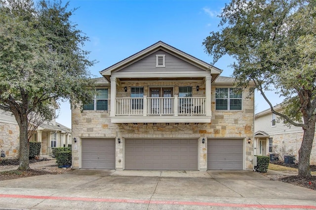 view of front of property featuring an attached garage, central AC, a balcony, stone siding, and driveway