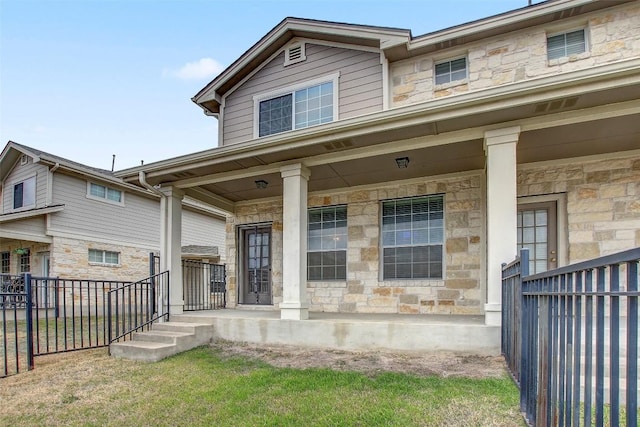 view of front of property with covered porch, stone siding, and fence