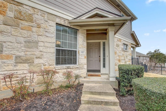 entrance to property featuring stone siding and fence