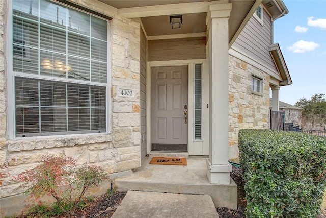 view of exterior entry featuring stone siding and fence