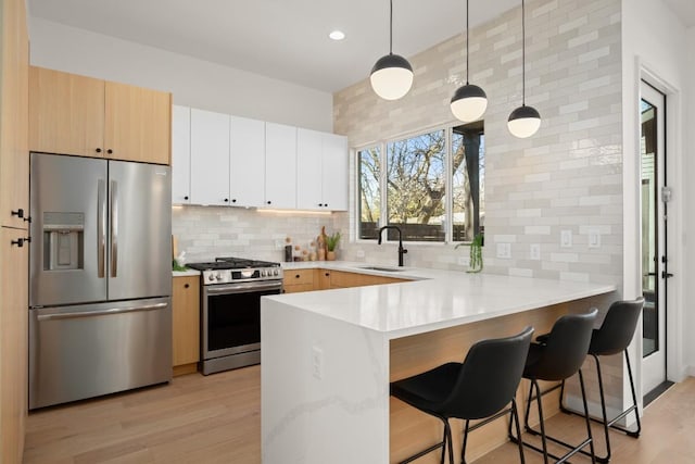 kitchen with a peninsula, stainless steel appliances, light countertops, a kitchen bar, and a sink