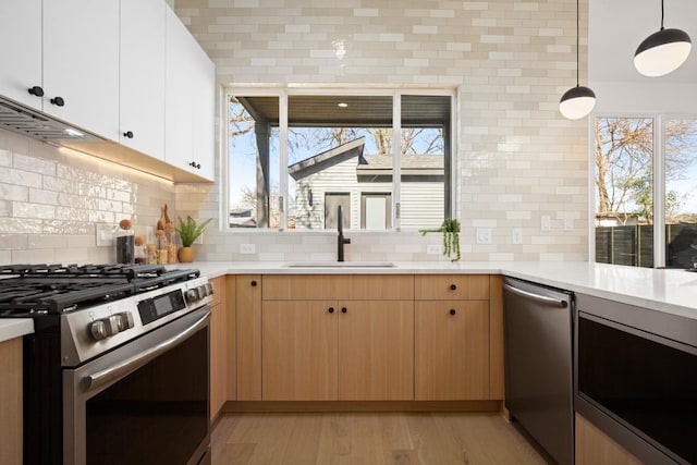 kitchen featuring a sink, light countertops, appliances with stainless steel finishes, light wood-type flooring, and tasteful backsplash