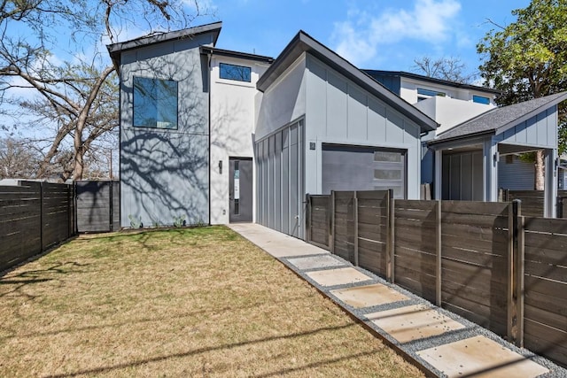 view of front facade with board and batten siding, fence private yard, an attached garage, and a front yard