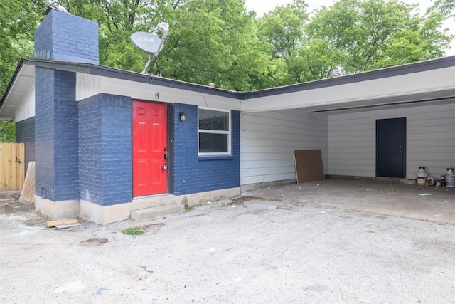 view of front facade featuring entry steps, a chimney, a carport, and brick siding