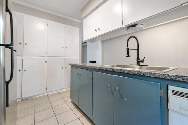 kitchen featuring crown molding, light tile patterned floors, freestanding refrigerator, white cabinetry, and a sink